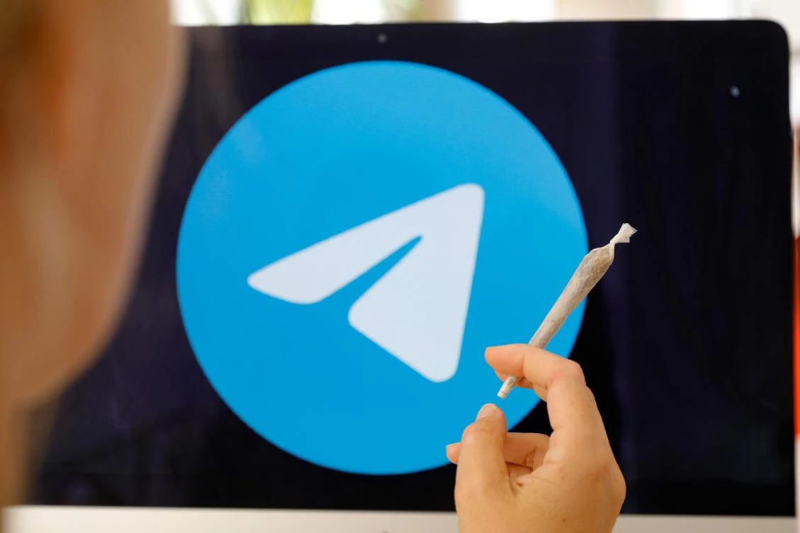 This illustration picture taken on August 16, 2019 in Paris shows a person posing with a hand-rolled cigarette in front of a screen showing the Telegram app logo. (AFP/Geoffroy Van Der Hasselt)