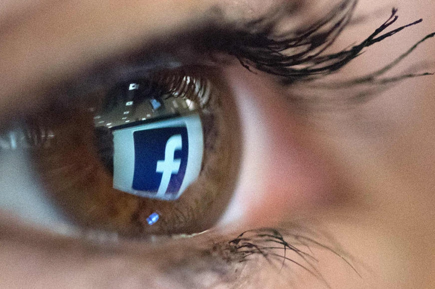 An illustration picture taken on March 22, 2018 in Paris shows a close-up of the Facebook logo in the eye of an AFP collaborator posing while she looks at a flipped logo of Facebook. (AFP / Christophe Simon)