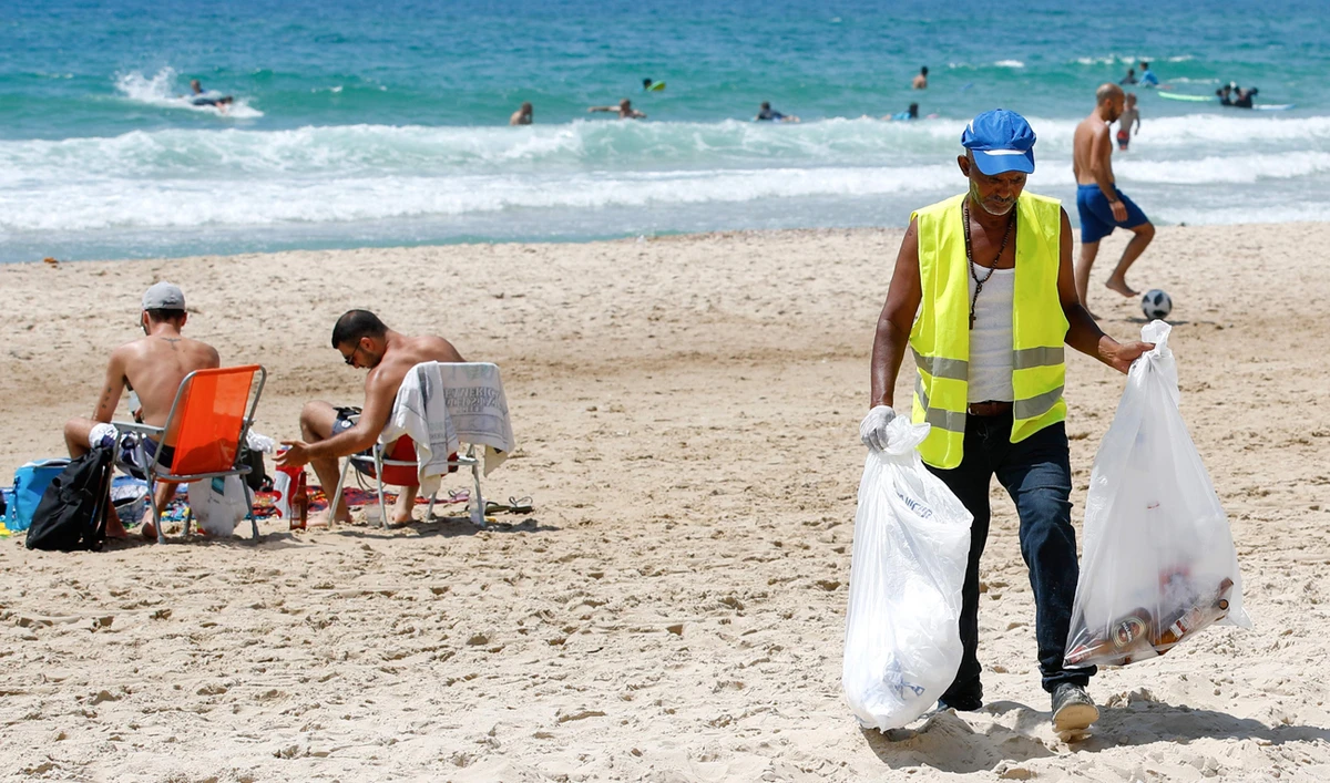 An employee of the Herzliya town hall collects plastics and other waste left behind by beachgoers. (AFP)