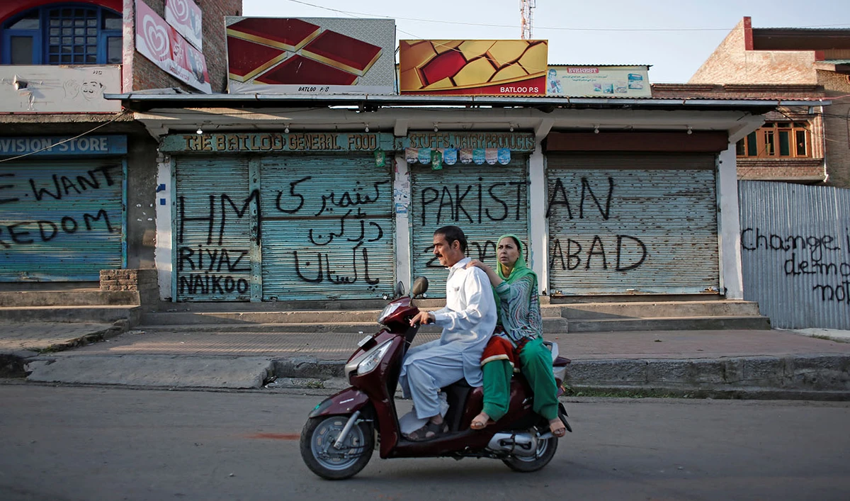 Kashmiris ride on a scooter past the closed shops painted with graffiti during restrictions, after scrapping of the special constitutional status for Kashmir by the Indian government, in Srinagar, Aug. 20, 2019. (REUTERS)