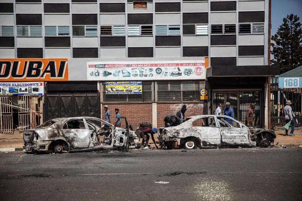 People rummage through a burned car in Johannesburg suburb of Malvern, on September 4, 2019, after South Africa's financial capital was hit by a new wave of anti-foreigner violence. (AFP)