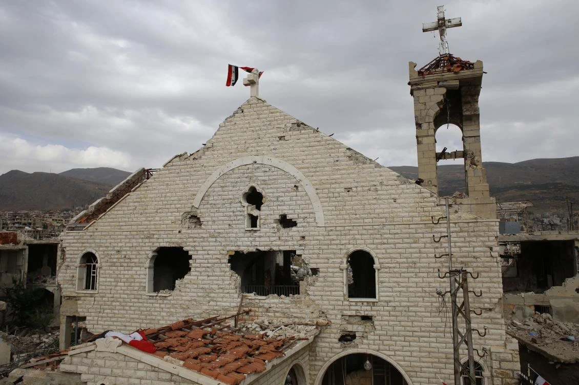 This May 18, 2017 file photo, shows a Syrian flag raised over the damaged Saint Mary Roman Orthodox church at the mountain resort town of Zabadani in the Damascus countryside, Syria. (AP Photo/Hassan Ammar, File)