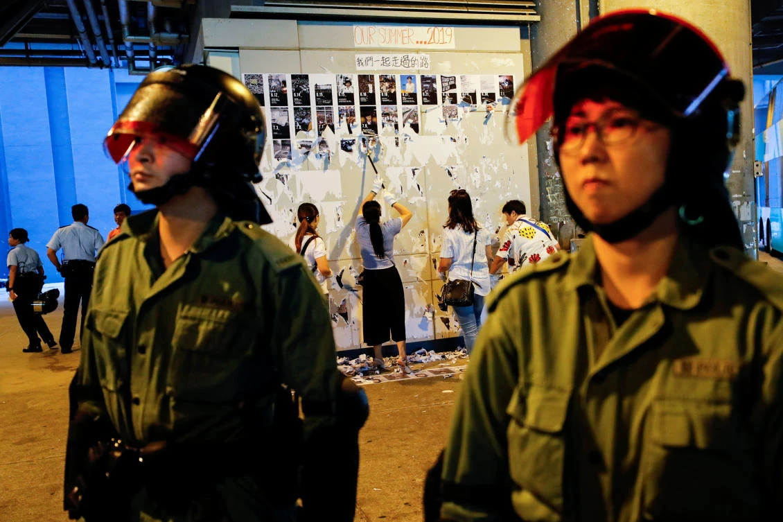 Riot police are seen in front of pro-China supporters as they pull down Lennon Walls of anti-government posters and memo outside Yuen Long MTR station in Hong Kong. (Reuters)