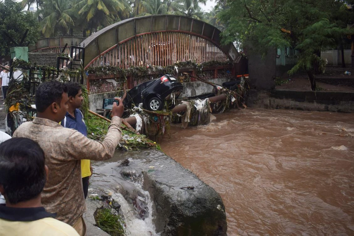 Onlookers and residents take photos of a car washed away by flash floods following heavy overnight rains in Pune on Sept. 26, 2019. (AFP)