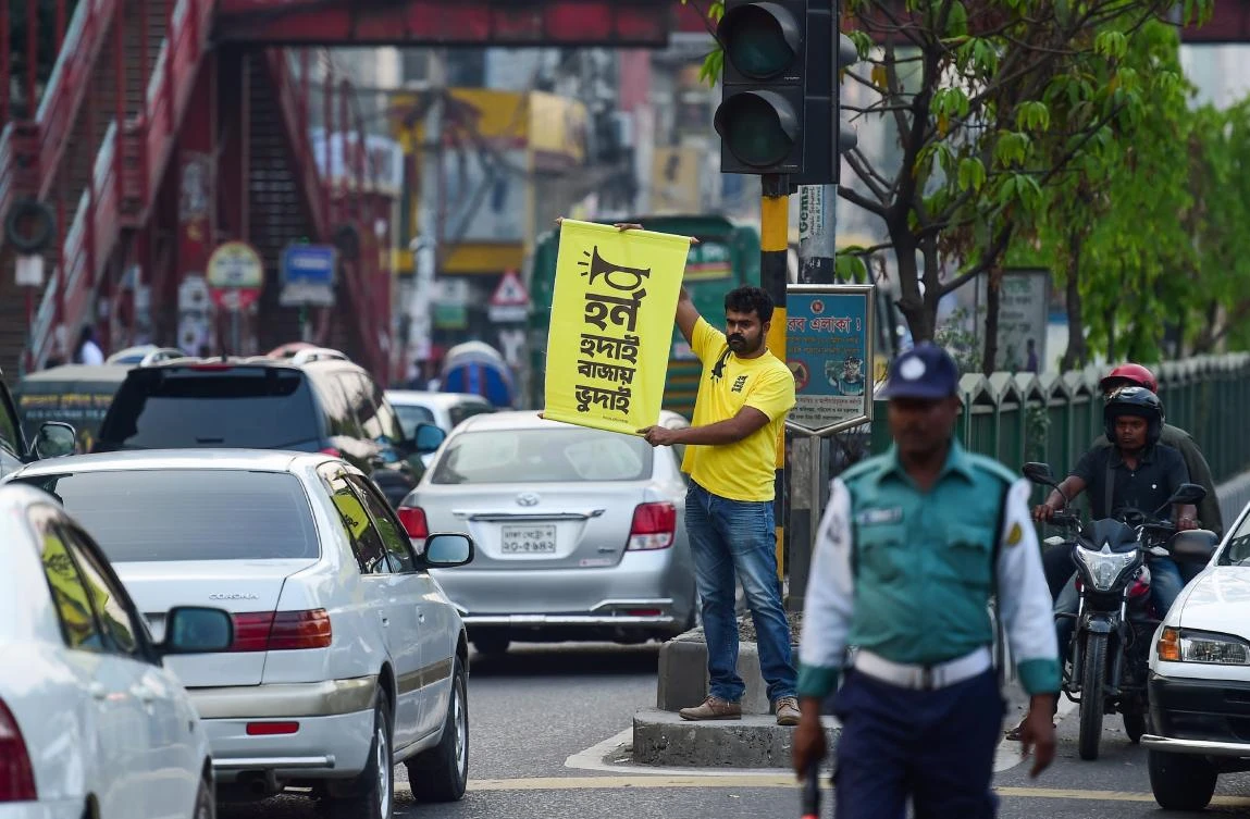 Mominur Rahman Royal stands at a busy intersection with a yellow placard with the Bengali rhyme “Horn Hudai, Bajay Bhudai” meaning “Only an idiot honks a horn unnecessarily.” (AFP)