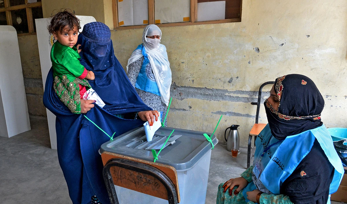 A woman holds her child as she casts her vote at a polling station in Jalalabad on Sept. 28, 2019. (AFP)