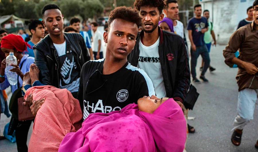 A migrant carries a woman during clashes with police outside the refugee camp of Moria on the Greek island of Lesbos, on September 29, 2019. (AFP)