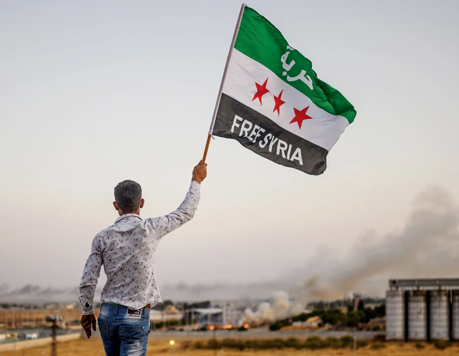 A man waves a Syrian opposition flag reading ‘Free Syria’ on Sunday in Akcakale as smoke rises in the background. (AFP)