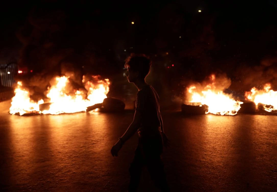 A Lebanese demonstrator walks past burning tires during a protest against recent tax calls on October 17, 2019 in the southern suburb of Beirut. (AFP)