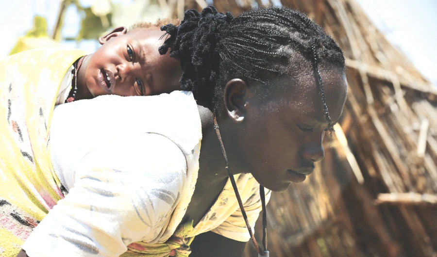 A Sudanese woman carries her baby on her back as she works in the village of Shattaya in Darfur region, following her return home after over a decade of being displaced. (AFP)