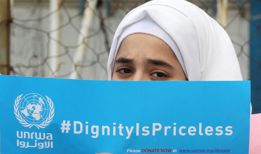 A Palestinian refugee holds a placard at a school belonging to the United Nations Relief and Works Agency for Palestinian Refugees (UNRWA) in the town of Sebline east of the southern Lebanese port of Saida, on March 12, 2018. (AFP)