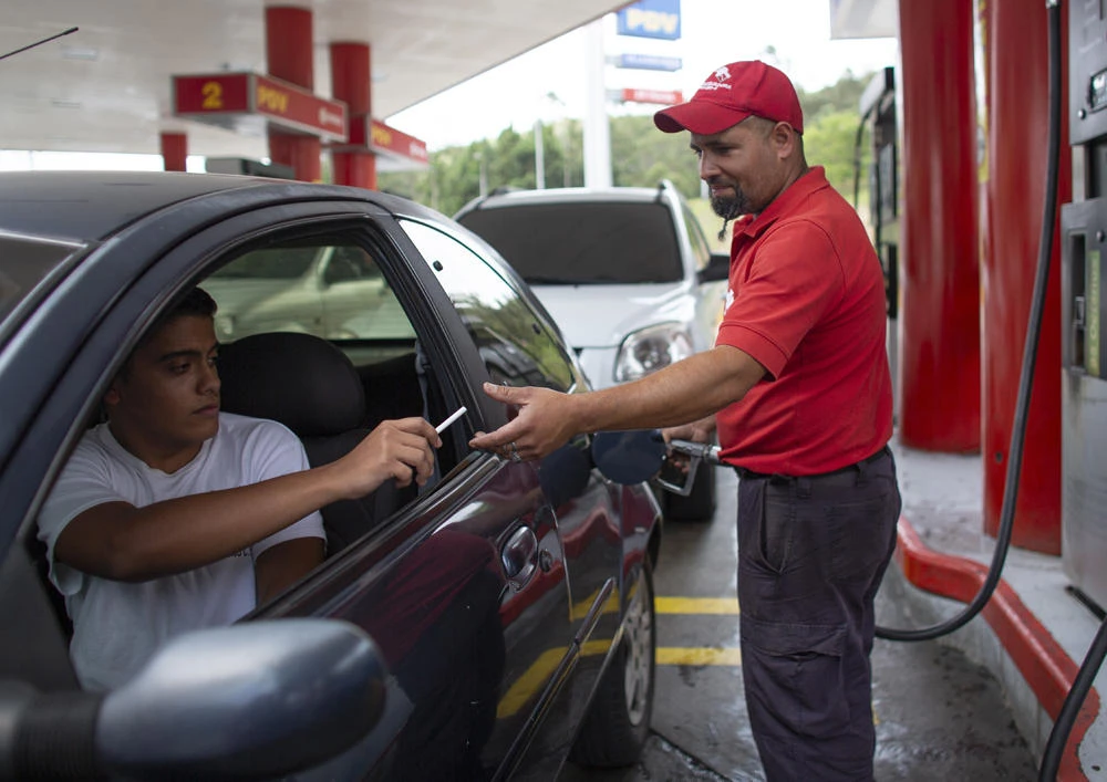 In this Oct. 8, 2019 photo, a gas station attendant takes a cigarette as payment from a motorist as he fills the tank in San Antonio de los Altos on the outskirts of Caracas, Venezuela. (AP Photo/Ariana Cubillos)