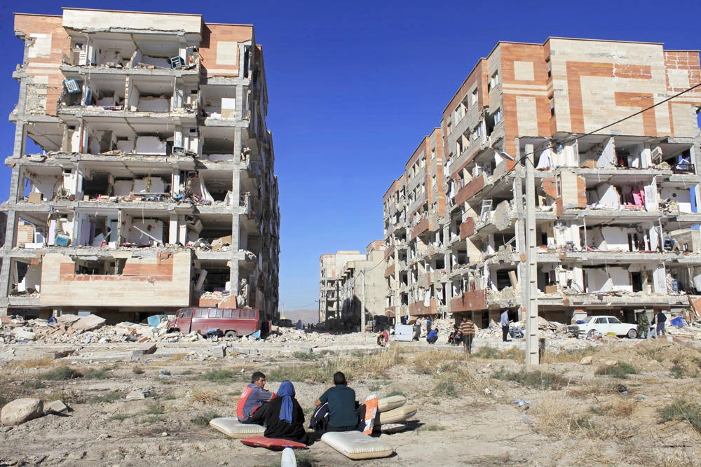 In this Nov. 13, 2017 file photo, survivors sit in front of buildings damaged by an earthquake, in Sarpol-e-Zahab, western Iran. A magnitude 5.9 earthquake hit northwestern Iran on Friday, killing at least five people and injured 120 others. (AP Photo/Omid Salehi)