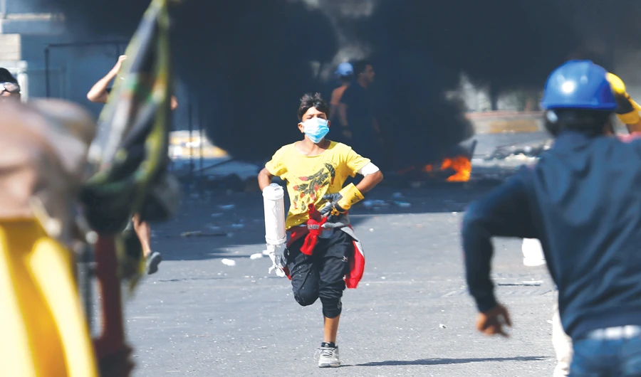 Demonstrators run after they set fire during the ongoing protests in Baghdad on Saturday. Nationwide rallies have brought Iraq to a standstill. (Reuters)