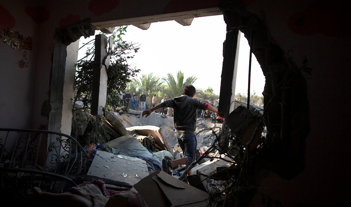 A Palestinian boy walks through a hole in a wall of a destroyed house following overnight Israeli missile strikes, in the town of Khan Younis, southern Gaza Strip. (AP)