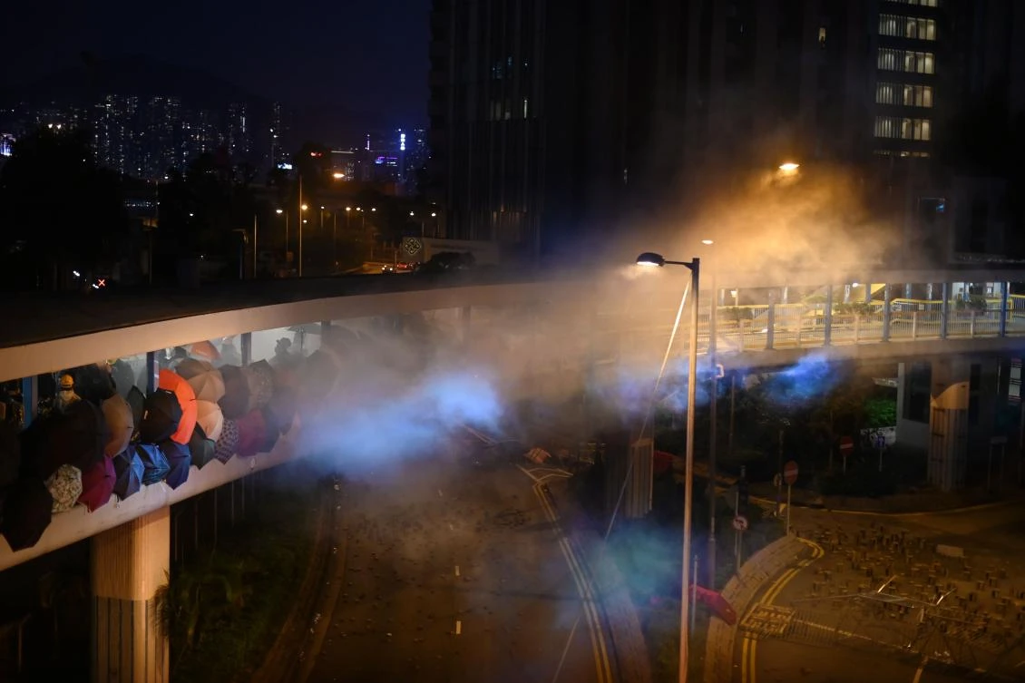 Anti-government protesters use umbrellas as shields to protect themselves from tear gas fired by the police on a highway bridge outside the Polytechnic University, in Hung Hom district of Hong Kong, on November 17, 2019. (AFP)