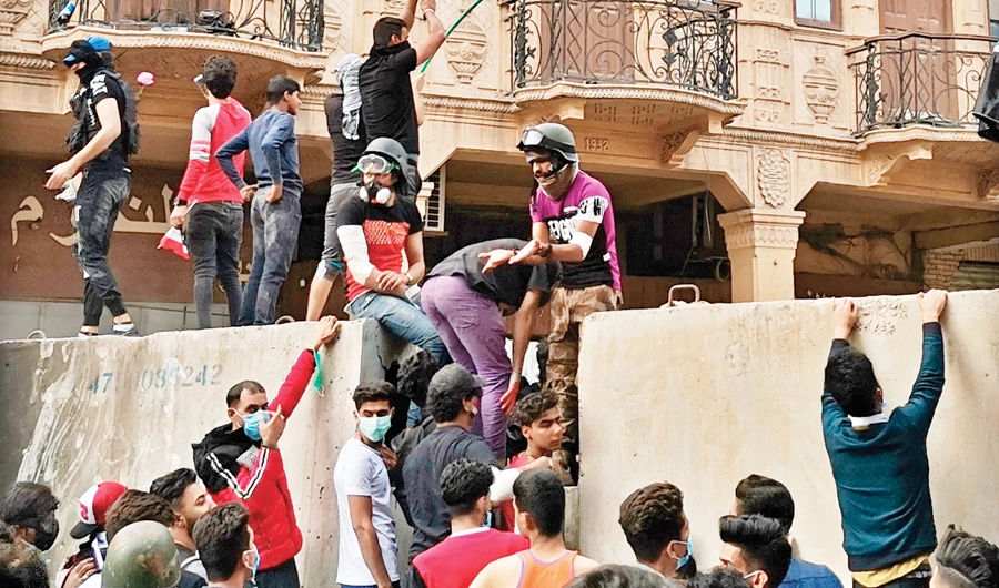 As strikes resume in Iraq, anti-government protesters stand on a concrete wall set up by security forces in Al-Rashid district in Baghdad on Sunday. (AP)