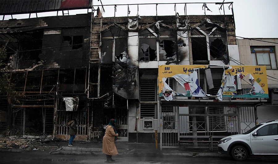 In this photo taken Monday, Nov. 18, 2019, and released by Iranian Students' News Agency, ISNA, people walk past buildings which burned during protests that followed the authorities' decision to raise gasoline prices, in the city of Karaj, west of the capital Tehran, Iran. (AP Photo)