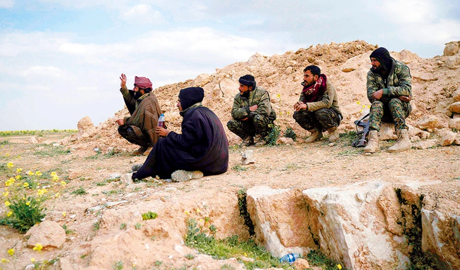 US-backed Syrian Democratic Forces (SDF) fighters sit atop a hill in the desert outside the village of Baghouz, Syria. (AP)