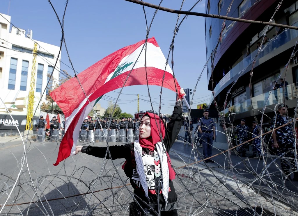 A Lebanese demonstrator waves the national flag while security forces stand by, during an anti-American protest near the US embassy in Awkar, northeast of the capital Beirut, on November 24, 2019. (AFP)