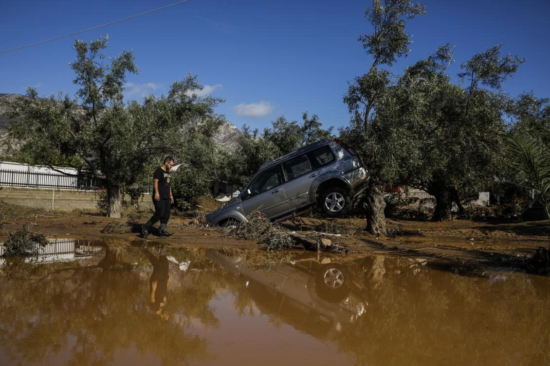 A man walks past a car moved by the force of flood water after storms in Kineta village, about 68 kilometers west of Athens. (AP Photo)