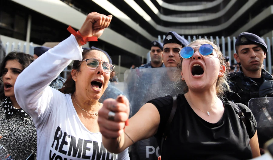 Protesters chant slogans during ongoing protests against the Lebanese political class, as riot police stand guard in front of Finance Ministry building in Beirut, Lebanon, on Friday. (AP)
