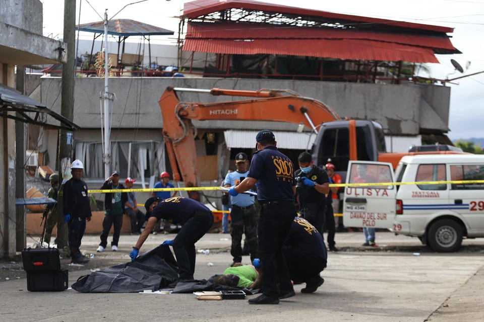 Police forensic investigators work over bodies retrieved from a collapsed building (background) in Padada town, Davao del Sur province on the southern island of Mindanao on Dec.16, 2019, following a 6.8-magnitude earthquak the day before. (AFP / Manman Dejeto)