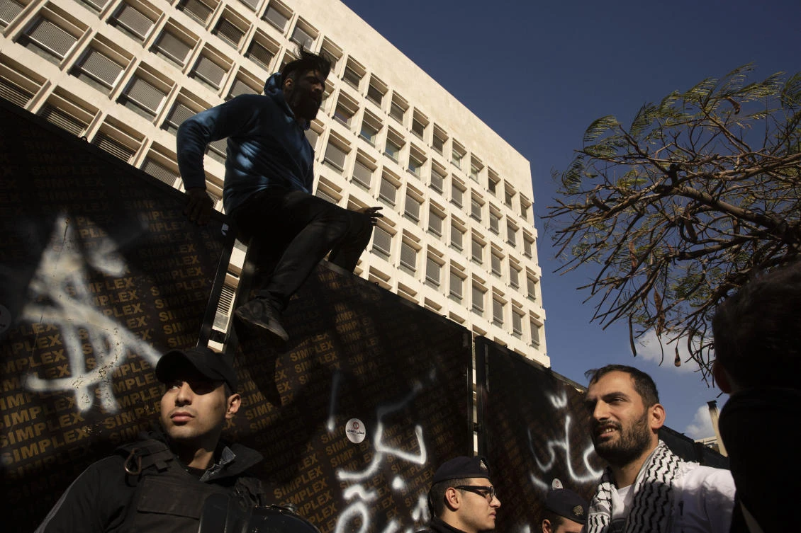 An Anti-government protester climbs down from a security barrier as dozens chant slogans outside of the central bank Tuesday, Dec. 24, 2019, in Beirut, Lebanon. (AP)