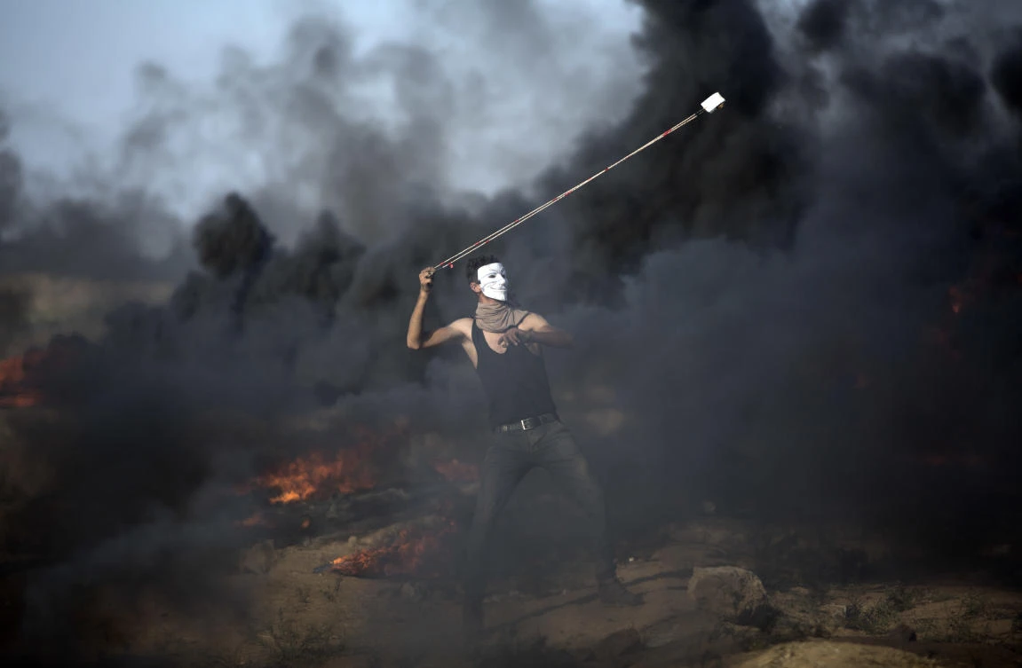 A Palestinian protester hurls stones at Israeli troops during a protest at the Gaza Strip’s border with Israel, Organizers of the weekly Palestinian demonstrations along the Gaza Strip’s frontier with Israel say they will significantly scale down the gatherings in 2020. (AP)