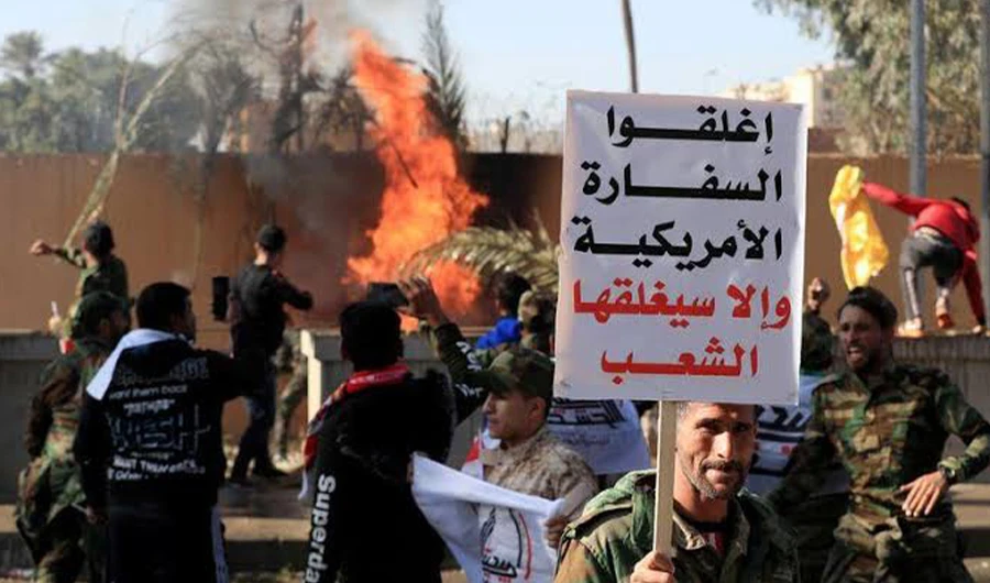A Hashd al-Shaabi fighter holds a sign reading "Close the American embassy otherwise people will close it", as others set fire on the U.S. Embassy wall to condemn air strikes on bases belonging to Hashd al-Shaabi (paramilitary forces), in Baghdad, Iraq December 31, 2019. (Reuters)