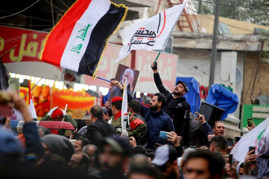 Mourners wave the national flag and the Hashed al-Shaabi flag as they carry the portrait Iraqi paramilitary chief Abu Mahdi al-Muhandis during a funeral procession, for Muhandis and Iranian military commander Qasem Soleimani, in Kadhimiya, a Shiite pilgrimage district of Baghdad, on January 4, 2020. (AFP)