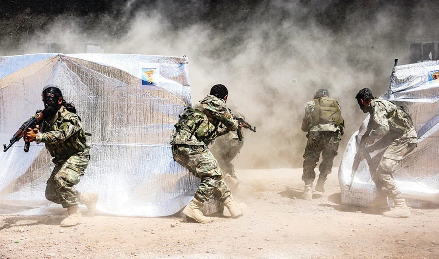 Turkish-backed Syrian fighters perform maneuvers past tents with posters showing the flags of the Kurdish People’s Protection Forces during a military exercise on Syria’s northern border with Turkey. (AFP)