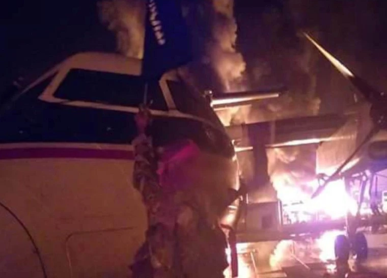 A militant holds the group’s flag next to a burning aircraft, said to be at the Manda Bay Airfield in Kenya, in this image distributed by the Al-Shabab group. (Al-Shabaab via Reuters)