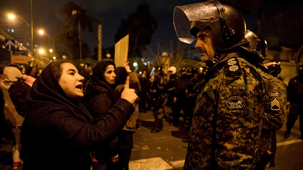 In this photo released by Iranian Students' News Agency, ISNA, a woman attending a candlelight vigil to remember the victims of the Ukraine plane crash, talks to a policeman, at the gate of Amri Kabir University in Tehran on Jan. 11, 2020. ISNA via AP)
