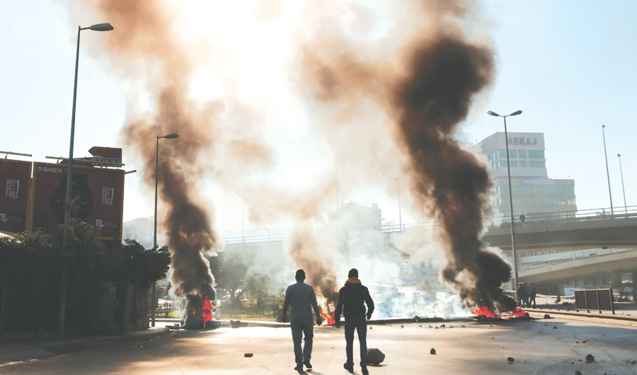 Men walk near burning tires set on fire by anti-government protesters after weeks of calm in Beirut, as demonstrators block several roads in the capital city. (AP)