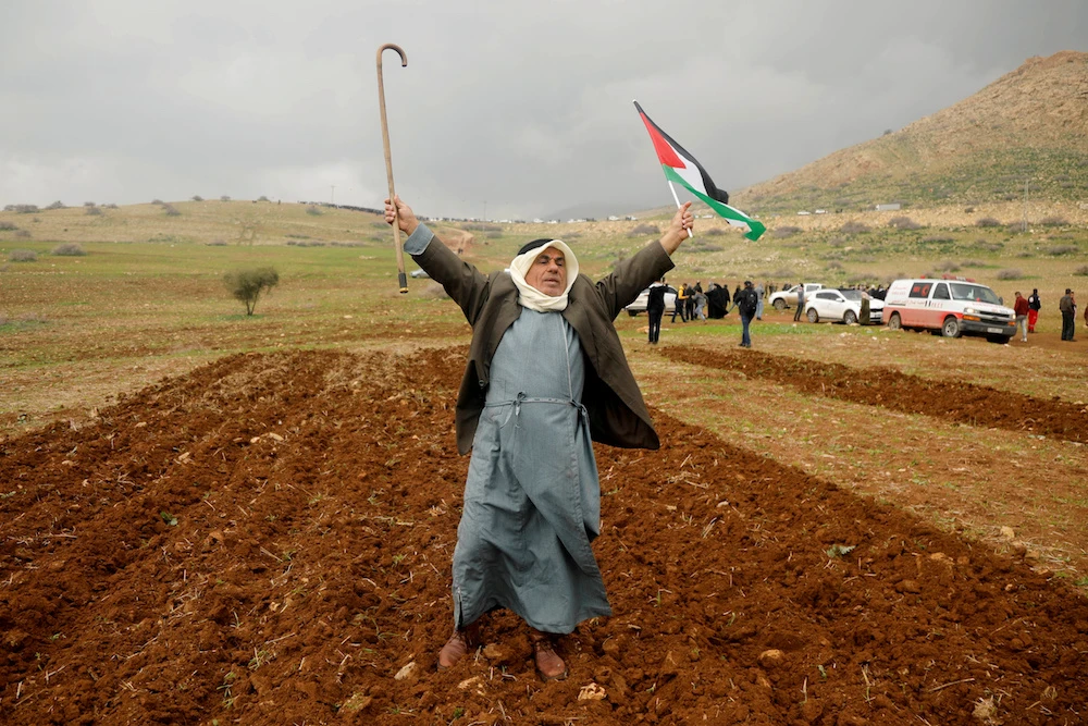 A demonstrator holds up a cane and a Palestinian flag during a protest against the US president Donald Trump’s Middle East peace plan, in Jordan Valley in the Israeli-occupied West Bank Jan. 29, 2020. (Reuters)
