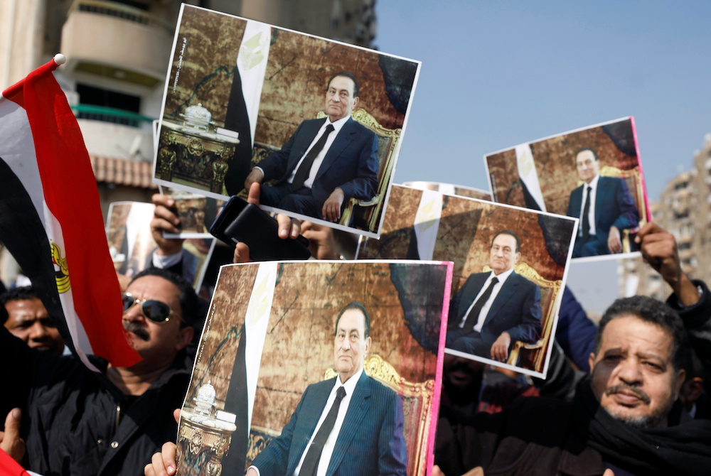 Supporters of former Egyptian President Hosni Mubarak hold his photos near the main gate of a cemetery during his burial ceremony, east of Cairo. (Reuters)