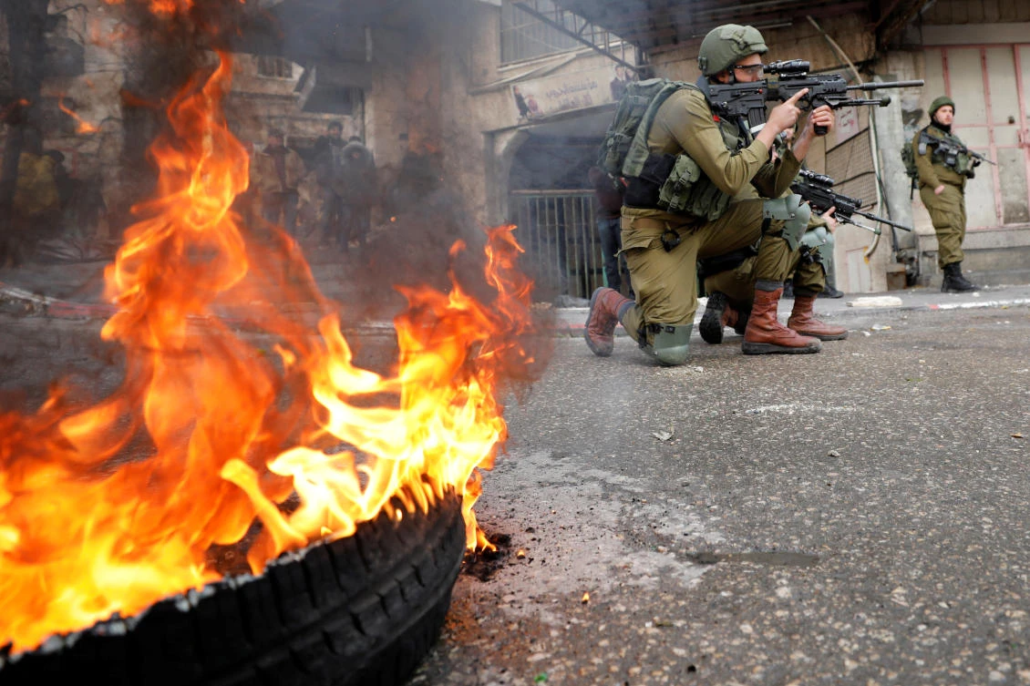 An Israeli soldier aims his weapon as a tire burns during a Palestinian protest against the Middle East peace plan, in Hebron in the Israeli-occupied West Bank Jan. 31, 2020. (Reuters)