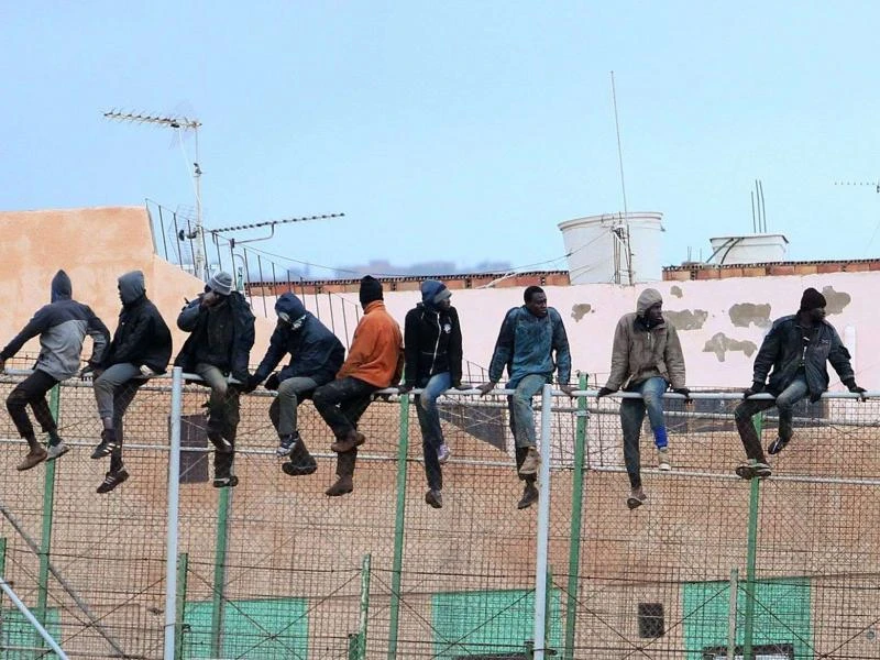 Migrants sit atop a border fence separating Morocco from the north African Spanish enclave of Melilla in an attempt to jump. (AFP)