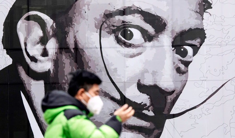An image of Salvador Dali looms over a man wearing a protective face mask at a shopping mall in Shanghai. China’s economy faces increasing disruption a month after the coronavirus outbreak which has claimed 636 victims. (AFP)