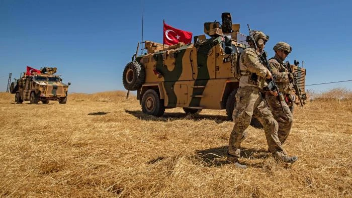 US soldiers walk past Turkish armored vehicles during a joint US-Turkey patrol in Syria, in 2019. (Reuters)