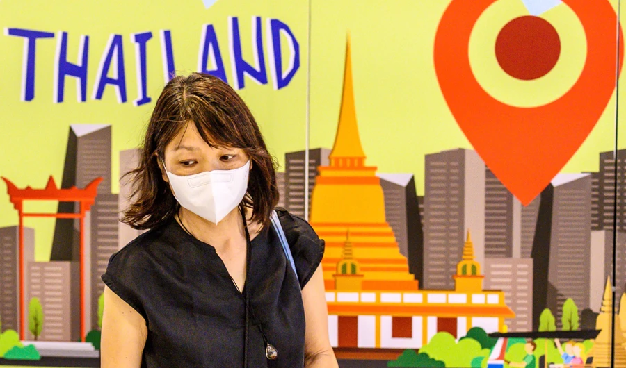 A woman, wearing a protective facemask amid fears over the spread of the COVID-19 coronavirus, walks in front of an advertisement board in Bangkok on February 17, 2020 featuring attractions in Thailand. (AFP)