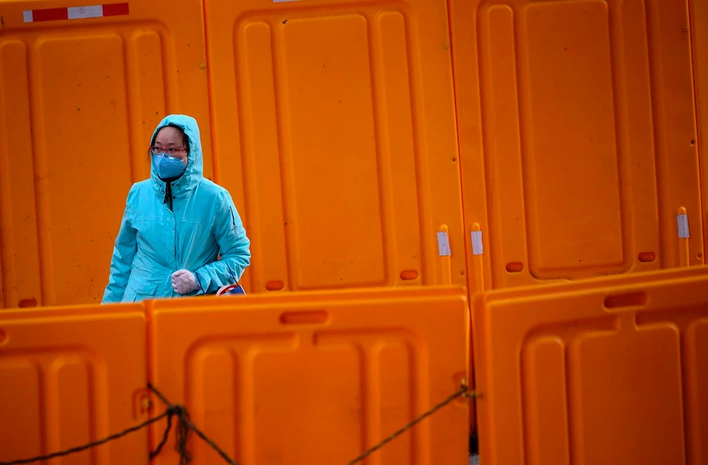 A woman wearing a protective facemask walks past construction barriers along a street in Shanghai on February 19, 2020. (AFP)