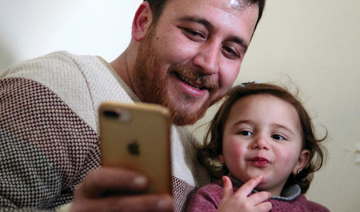 Syrian father Abdullah Al-Mohammed checks a phone with his three-year-old daughter Salwa at their home in Sarmada, a town in the Idlib province on Wednesday. (AFP)