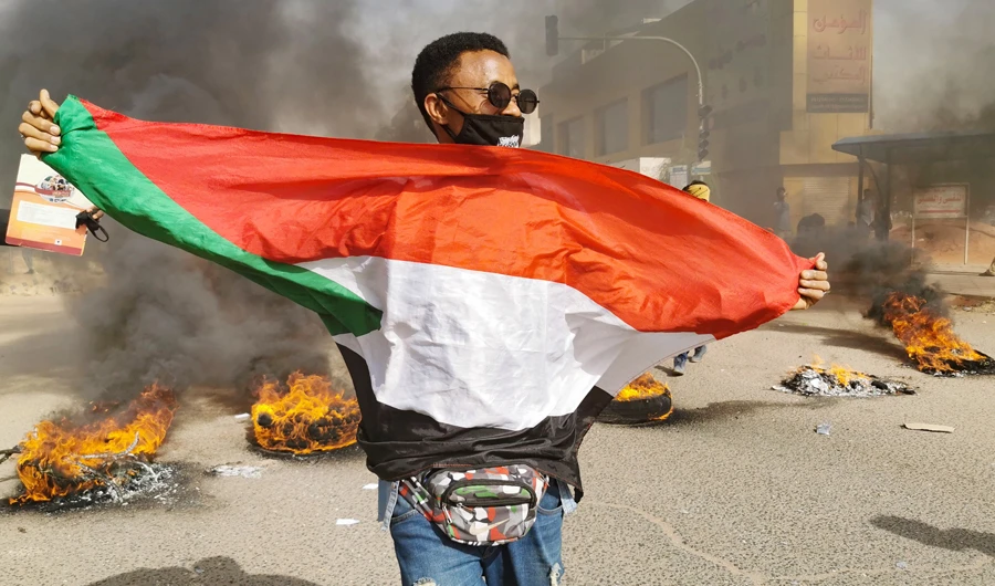 A Sudanese protestor carries a national flag as others burn tyres in the centre of the capital Khartoum during a demonstration calling for the reinstatement of soldiers who were forced into retirement after they voiced support for last year's revolution, on February 20, 2020. (AFP)