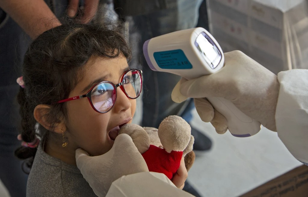 A member of a medical team takes a the temperature of a young Iraqi traveler at the Shalamjah border crossing upon her return from Iran on February 21, 2020. (AFP)