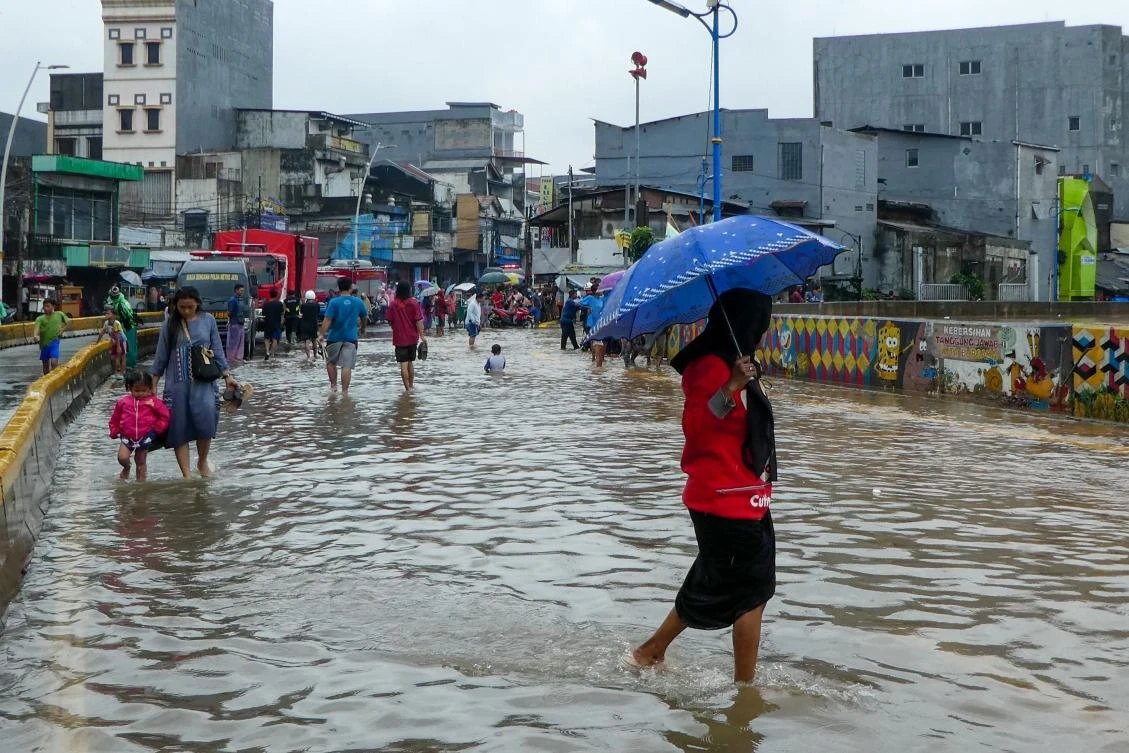 People walk through a flooded road after heavy rain in Jakarta on February 25, 2020. Dozens of Jakarta neighborhoods were flooded February 25 after torrential rains pounded Indonesia’s capital, less than two months after nearly 70 people were killed in some of the megacity’s worst flooding in years. (AFP)