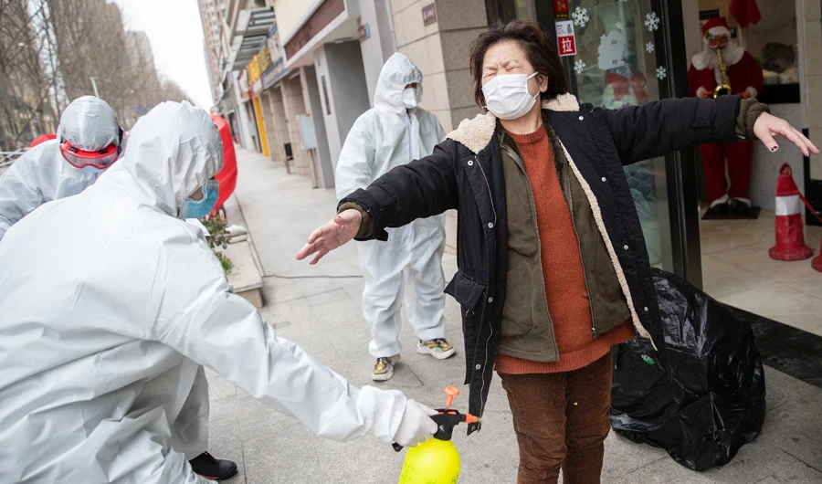 A woman (R), who has recovered from the COVID-19 coronavirus infection, is disinfected by volunteers as she arrives at a hotel for a 14-day quarantine after being discharged from a hospital in Wuhan, in China's central Hubei province on March 1, 2020. (AFP)