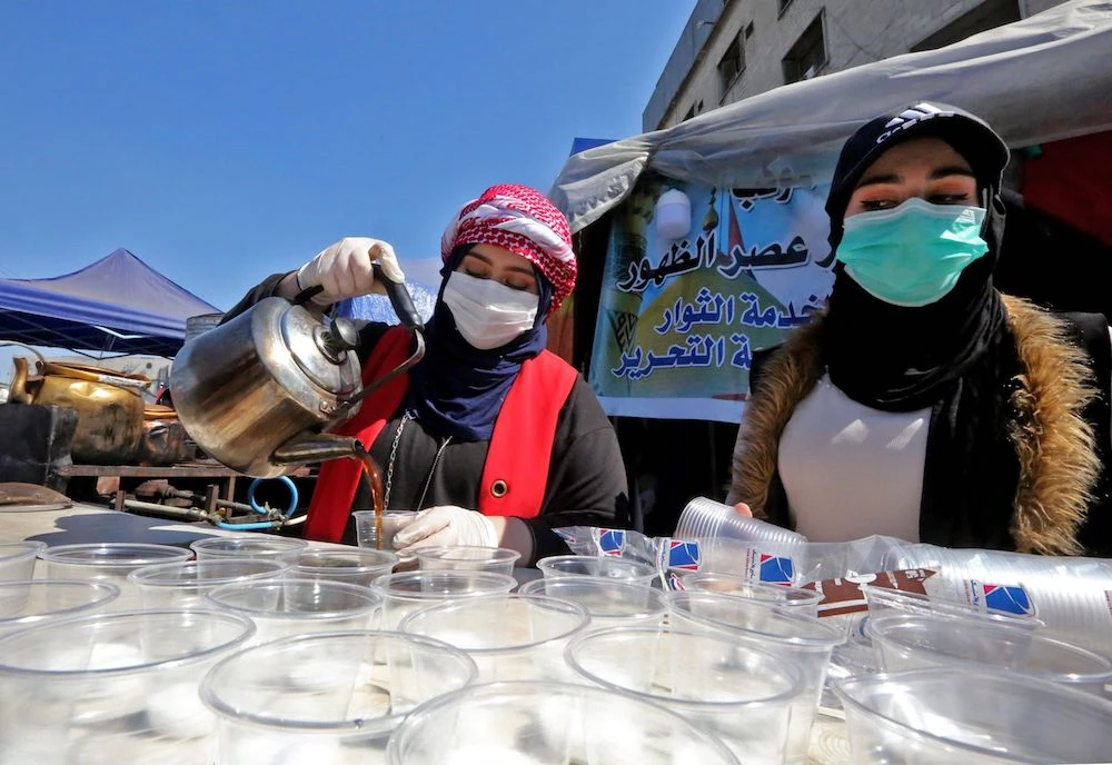 Iraqi women wearing protective masks a serve tea in Baghdad's Tahrir square where anti-government protesters continue their demonstrations. (AFP)