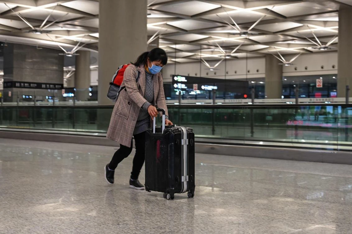 A passenger wearing a face mask walks with a broken luggage from Hongqiao International Airport to the Hongqiao Railway Station in Shanghai on Mar. 5, 2020. (AFP)